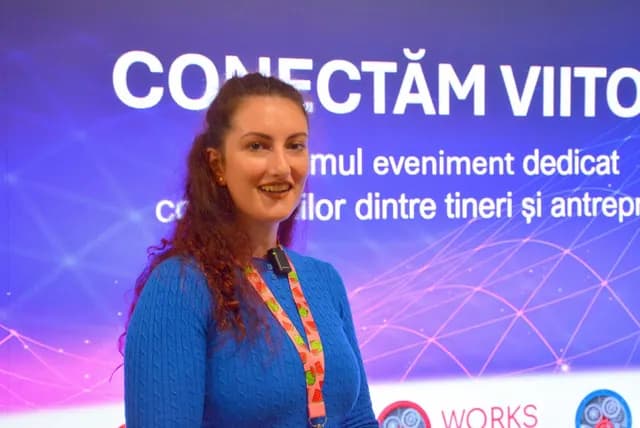 O participantă în pulover albastru zâmbește lângă ecranul Conectăm Viitorul.
