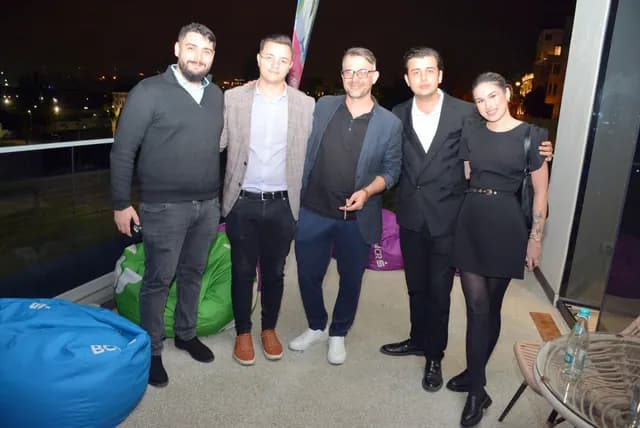 Cinci participanți pozează împreună lângă ferestrele Zbor Hub, seara.