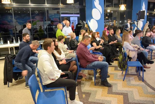 Participanți așezați în rânduri la Zbor Hub, înaintea unei prezentări.