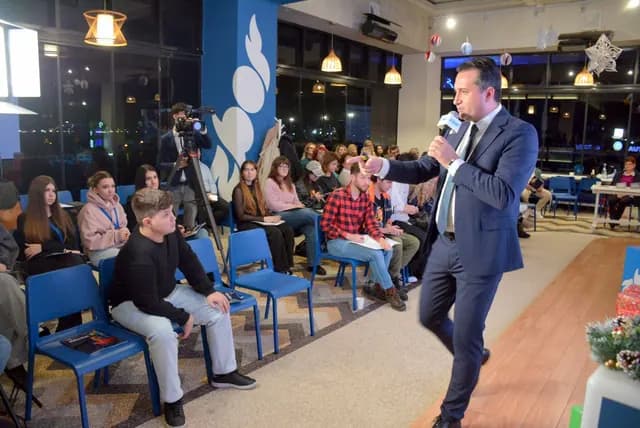 Un vorbitor vorbește la microfon aproape de primele rânduri ale publicului.