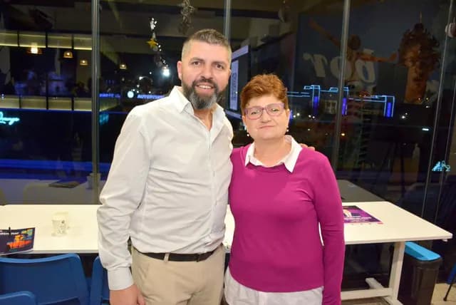 Doi participanți zâmbesc pentru o fotografie în sala de eveniment.