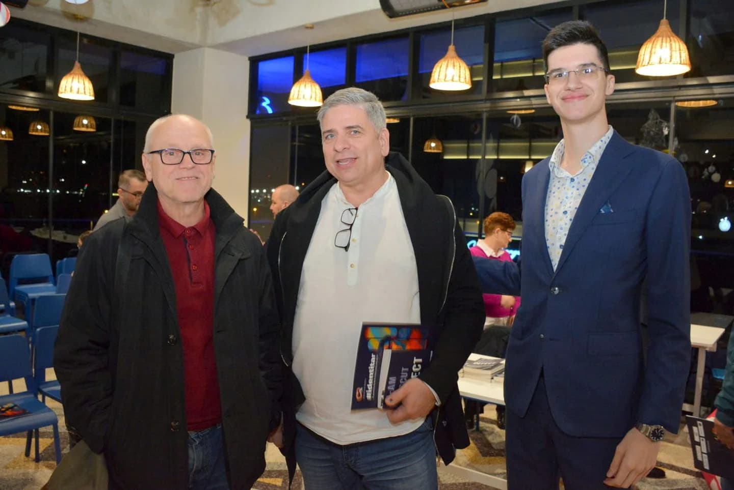 Trei participanți pozează în sala Zbor Hub; unul ține o carte.